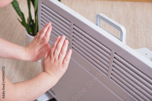 a small child warms his hands by the electric radiator in the room