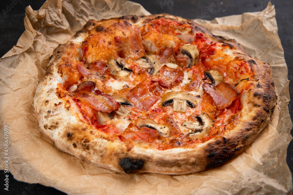 Delicious pizza with bacon and mushrooms mushrooms fresh Pastries on a black concrete background. Top view of a hot pepperoni pizza. With space for text. He was lying flat. Ruddy dough on kraft paper 
