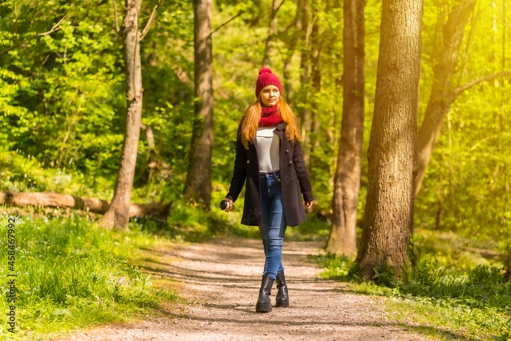 Latin girl with a black jacket, scarf and red woolen hat enjoying in an autumn park, walking along a path