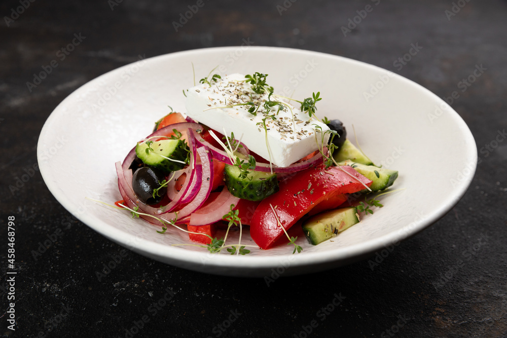 Greek salad with Feta cheese, red onion, tomatoes , cucumbers , olive oil, close-up, olives, in a white plate on a black background frame from above 