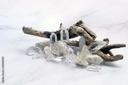 set of clear quartz minerals and dry tree branch on abstract marble background. gemstones crystals for esoteric spiritual practice, relaxation, meditation. reiki healing therapy for life balance