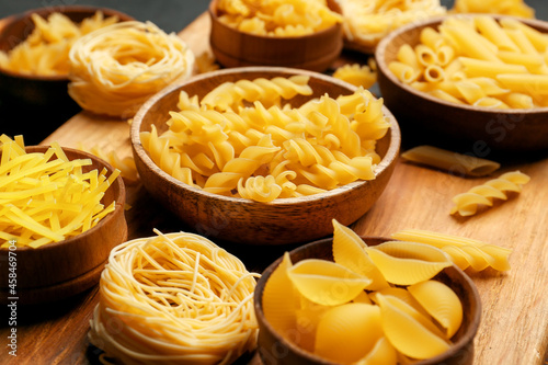 Bowls with different types of uncooked pasta on wooden background