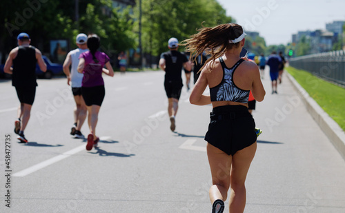 Woman in sportswear running city marathon and recording voice message on smartphone. One of contestants needing medical help. Concept of sport