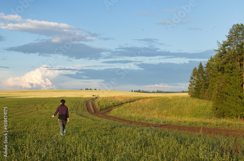 A girl walking in a clover field, a forest on the horizon