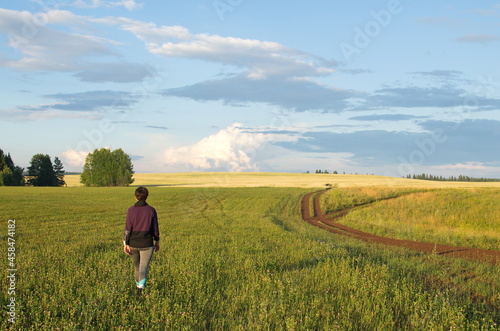 A girl walking along a field of clover, against a background of blue sky and clouds
