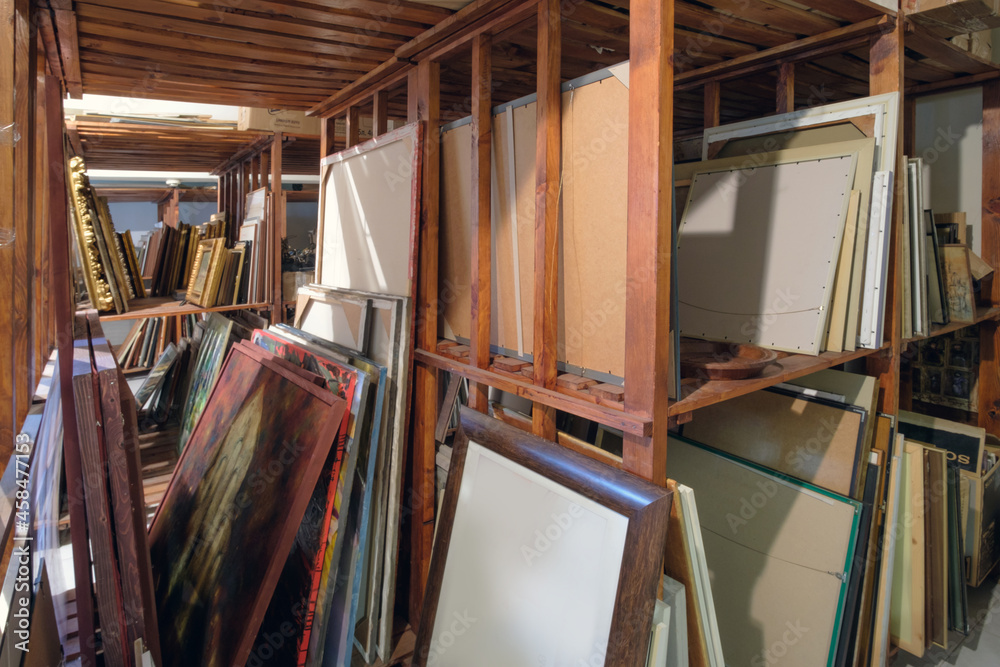 Wooden shelves full of pictures, frames and art equipment. Art gallery storage