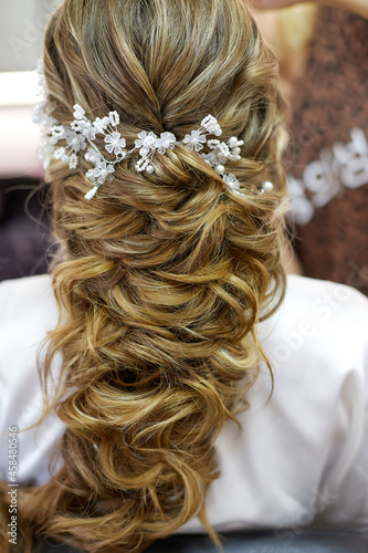 Blond Hair. Beautiful Caucasian Woman with Curly Long Hair. Bridal hairstyle decorated by white flowers