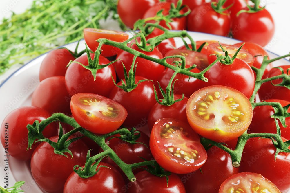 Composition from a plate full of branches of ripe fresh cherry tomatoes with spices on a wooden background Composition from a plate full of branches of ripe fresh cherry tomatoes with spices on a wooden background
