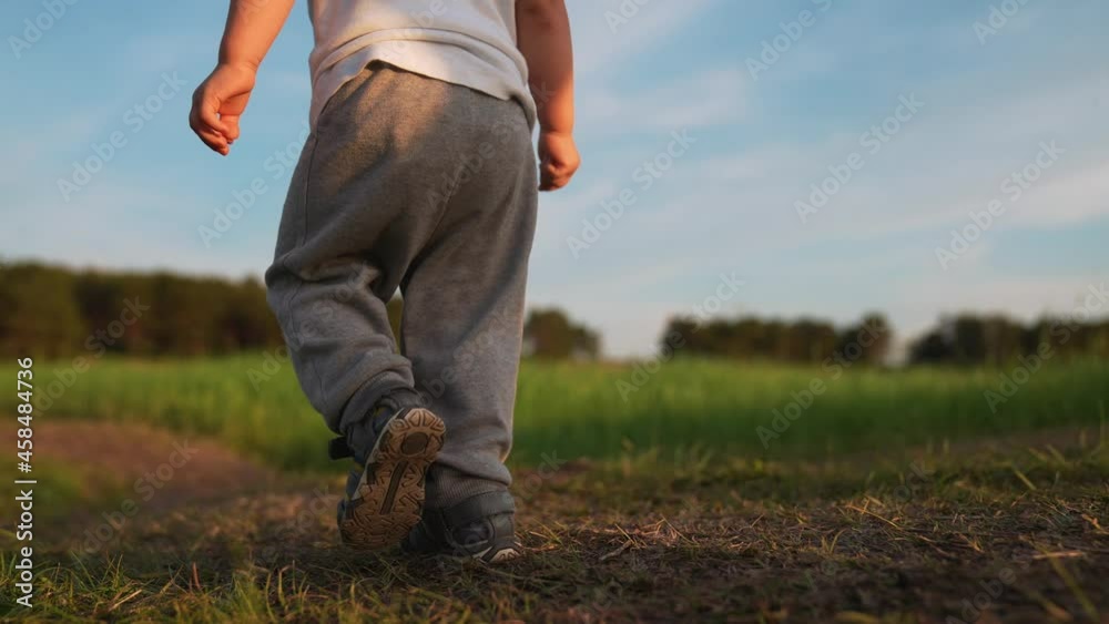Happy kid walks on green grass. Child takes the first steps along rural road. Kid run in nature in park. Boy walks on grass in field. Happy childish dream concept in park. Boy run on green grass