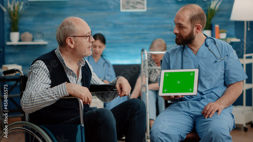 Man nurse and old patient looking at green screen on tablet in nursing home. Specialist holding horizontal chroma key with mockup template and isolated background. Medical assistant with device
