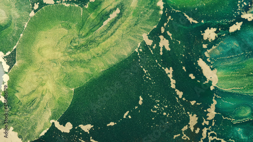 Gold green ink abstract, close-up. Shiny art dynamic green tide fluid paints. Texture of golden emerald flowing glitter. Watercolor liquid background. Green tide backdrop