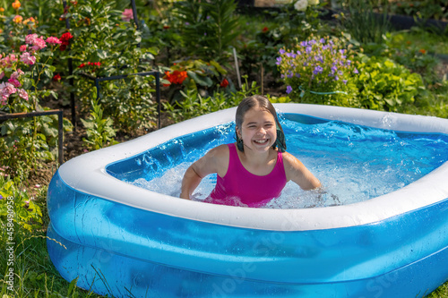 A girl in a pink bathing suit bathes in a blue inflatable pool in a blooming garden