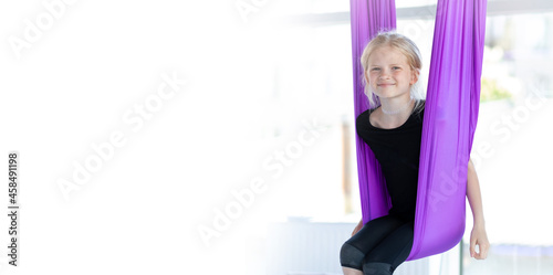 Banner kids Aerial flying yoga exercises. Portrait young smiling girl practice in stretching swing in purple hammock in fitness club. Copyspace.