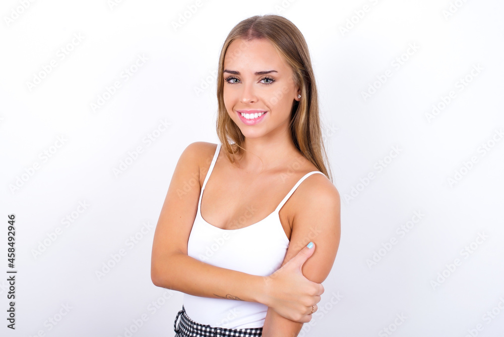 People, lifestyle, youth and happiness concept. Shy pretty beautiful blonde girl wearing sexy t-shirt on white background, feeling happy hugging herself. People, lifestyle, youth and happiness concept. Shy pretty beautiful blonde girl wearing sexy t-shirt on white background, feeling happy hugging herself.