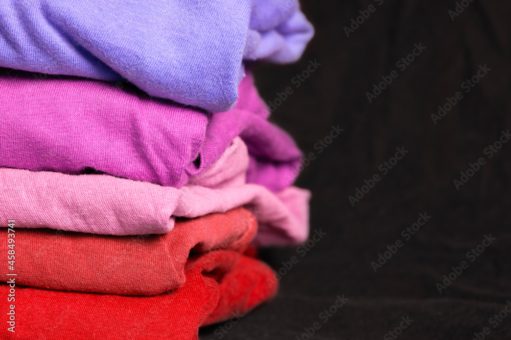 A stack of multi-colored fabric in warm colors. Background with folded clothes in red and lilac tones with empty space for information. T-shirts of different colors A stack of multi-colored fabric in warm colors. Background with folded clothes in red and lilac tones with empty space for information. T-shirts of different colors