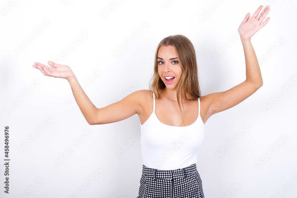 Cheerful beautiful blonde girl wearing sexy t-shirt on white background making a welcome gesture raising arms over head. Cheerful beautiful blonde girl wearing sexy t-shirt on white background making a welcome gesture raising arms over head.
