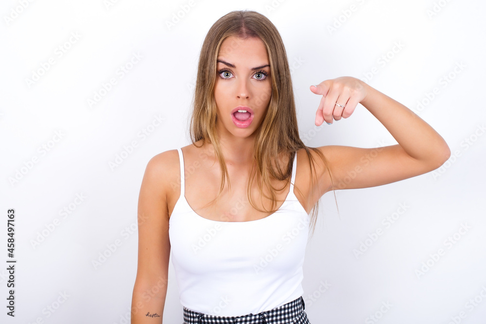 Shocked beautiful blonde girl wearing sexy t-shirt on white background points front with index finger at camera and. Surprise and advertisement concept. Shocked beautiful blonde girl wearing sexy t-shirt on white background points front with index finger at camera and. Surprise and advertisement concept.