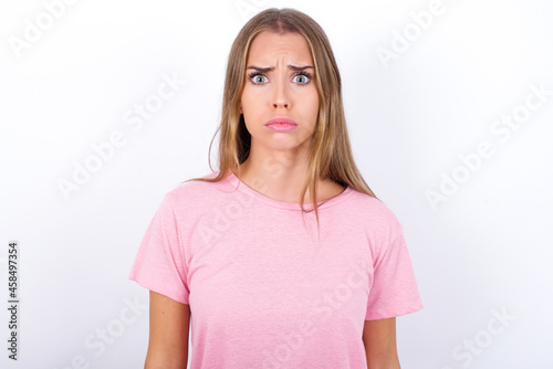 beautiful blonde girl wearing pink t-shirt on white background expressing disgust, unwillingness, disregard having tensive look frowning face, looking indignant with something.