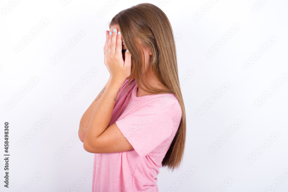 Sad beautiful blonde girl wearing pink t-shirt on white background covering face with hands and crying. Sad beautiful blonde girl wearing pink t-shirt on white background covering face with hands and crying.