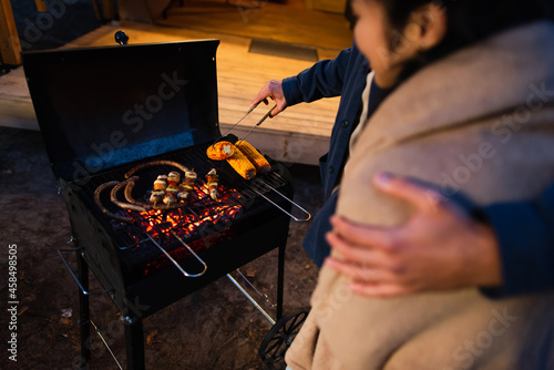 Cropped view of man cooking on grill and hugging blurred girlfriend outdoors