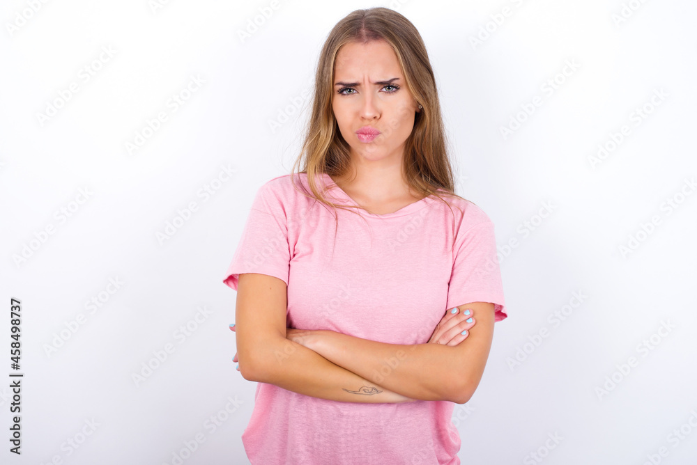 Picture of angry beautiful blonde girl wearing pink t-shirt on white background crossing arms. Looking at camera with disappointed expression. Picture of angry beautiful blonde girl wearing pink t-shirt on white background crossing arms. Looking at camera with disappointed expression.