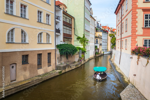Sticker Certovka, cruise boat with tourists sailing between buildings on water canal in