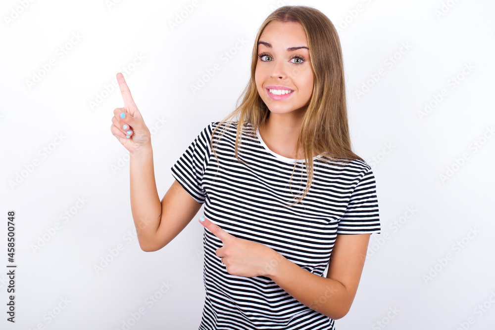 beautiful blonde girl wearing striped t-shirt on white background points at copy space indicates for advertising gives right direction beautiful blonde girl wearing striped t-shirt on white background points at copy space indicates for advertising gives right direction