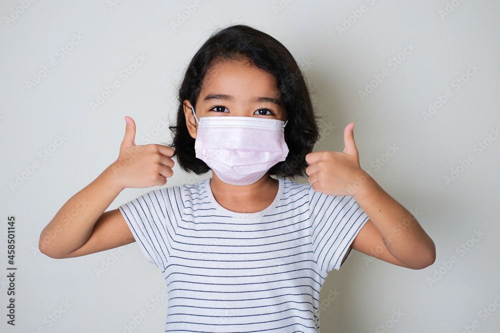 Asian little girl wearing protective medical mask while giving two thumbs up Asian little girl wearing protective medical mask while giving two thumbs up