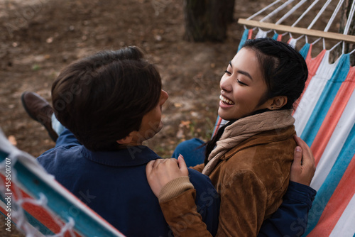 Asian woman hugging boyfriend in blurred hammock during vacation