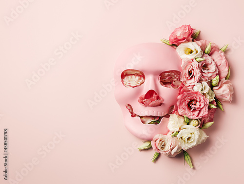 Fototapeta Naklejka Na Ścianę i Meble -  Pink face skull mask with a flower arrangement isolated on a pastel pink background. Romantic roses and plastic human's head skeleton. Creative Halloween or Day of the Dead floral concept. Flat lay.