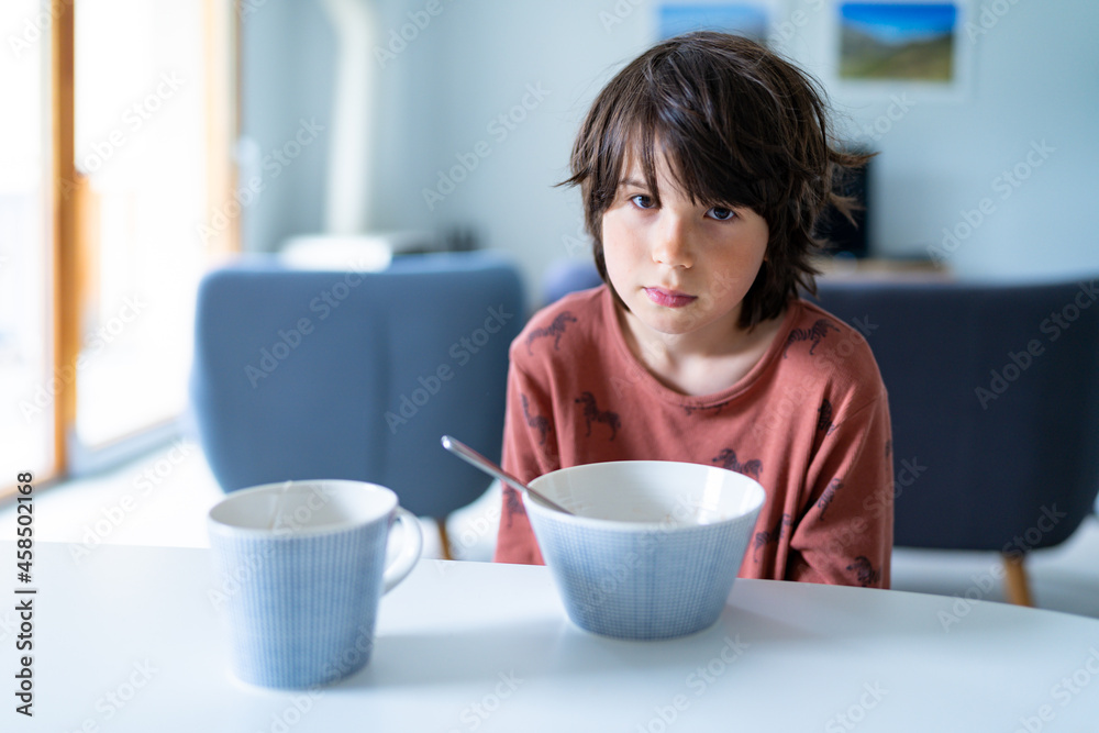 A young sleepy boy wearing pajamas taking breakfast at home in the morning before school. Healthy food for children. A young sleepy boy wearing pajamas taking breakfast at home in the morning before school. Healthy food for children.