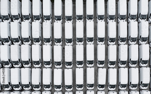 Aerial view of rows of new white vans parked together on a stockpile in vehicle manufacturing 
