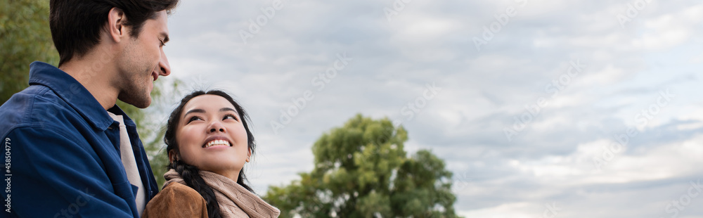 Smiling asian woman looking at boyfriend during weekend outdoors, banner Smiling asian woman looking at boyfriend during weekend outdoors, banner