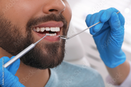 Dentist examining young man's teeth in clinic, closeup