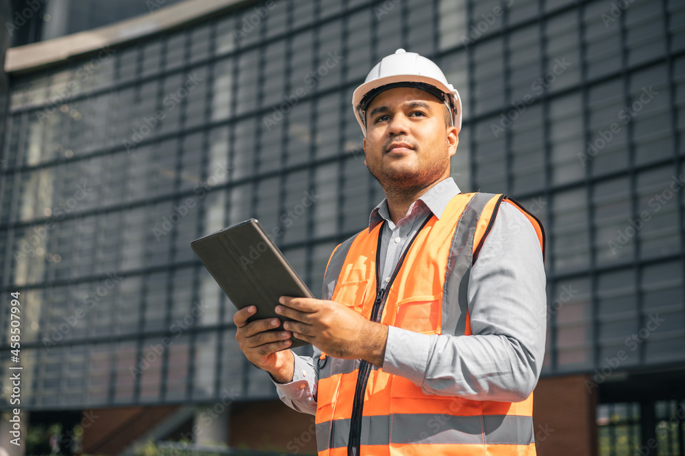 Young worker indian civil engineer using tablet planning the project build the modern construction reading the blueprint. Asian Architecture or engineer working in the building construction site. Young worker indian civil engineer using tablet planning the project build the modern construction reading the blueprint. Asian Architecture or engineer working in the building construction site.