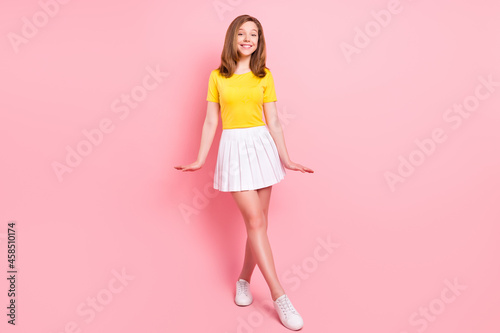 Full body photo of nice blond small girl wear yellow t-shirt skirt sneakers isolated on pink color background