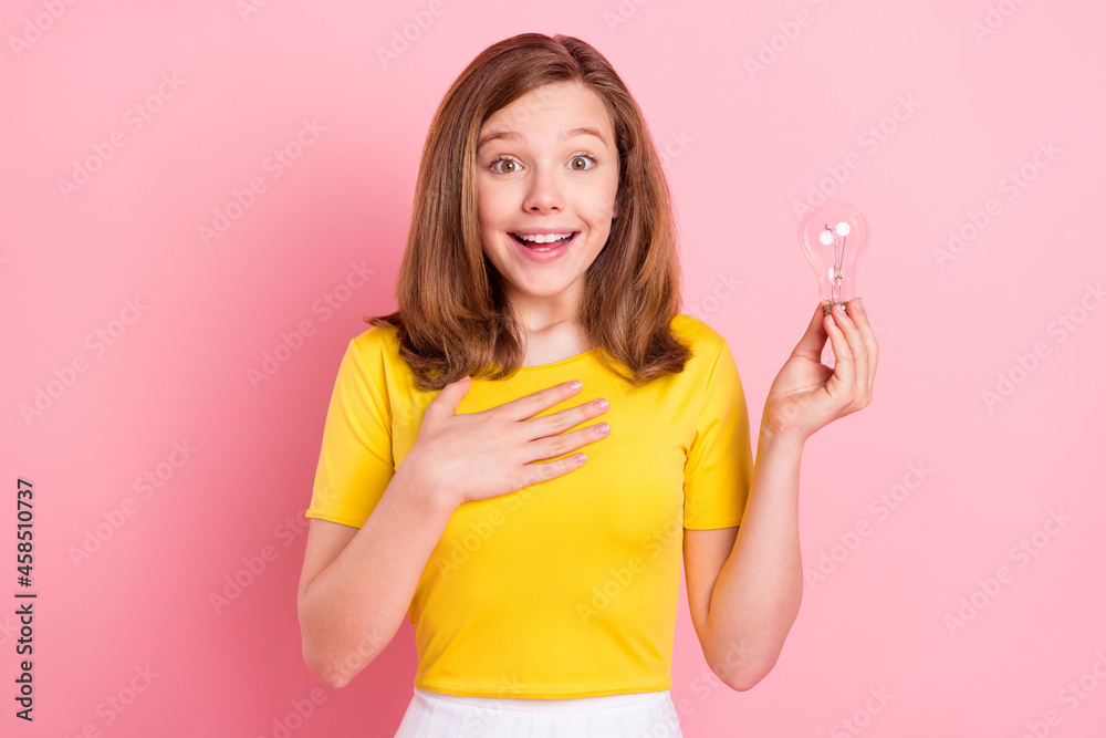 Photo of young girl happy positive smile amazed hand on chest hold light bulb creative idea isolated over pink color background