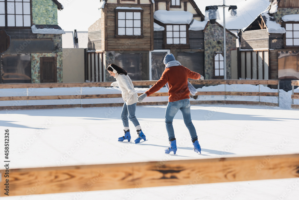 full length of happy couple skating on ice rink outside