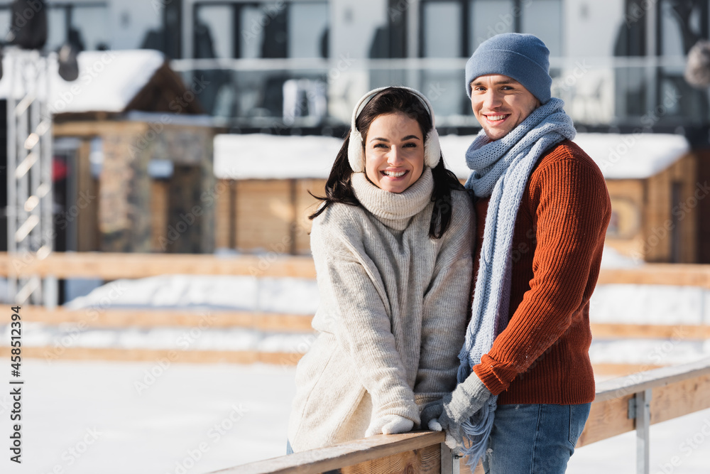 happy man and woman standing near wooden border on skating rink happy man and woman standing near wooden border on skating rink