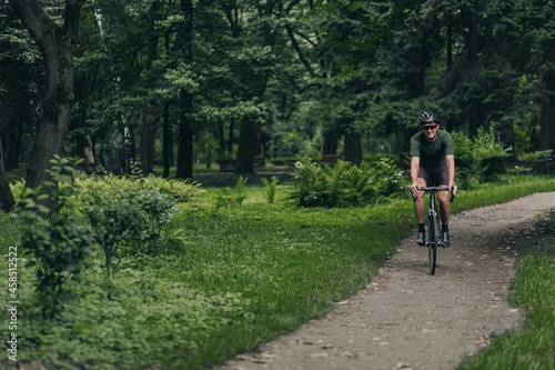 Positive man in sportswear riding bike at city park