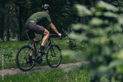 Muscular man using black bike for cycling on trail road