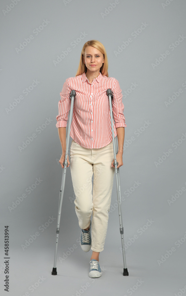 Young woman with axillary crutches on grey background Young woman with axillary crutches on grey background
