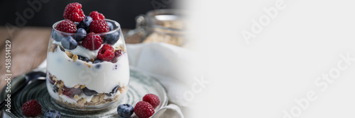 Granola parfait with berries and yogurt with a copy space. Parfait with granola , raspberries and blueberries on a white background with copy space. Granola in a glass . Food banner with granola 