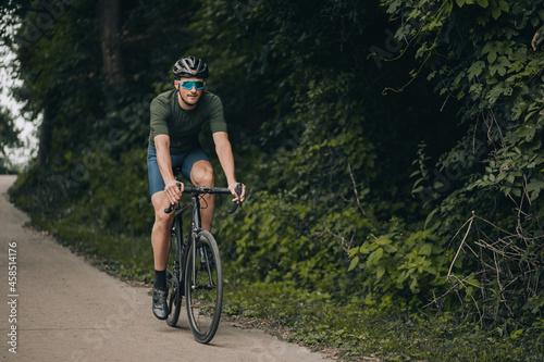 Muscular man in sport clothes riding bike at green park © Tymoshchuk