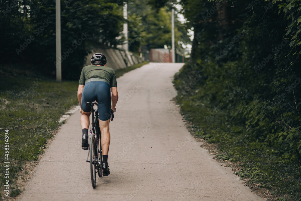 Back view of muscular man biking alone at green park