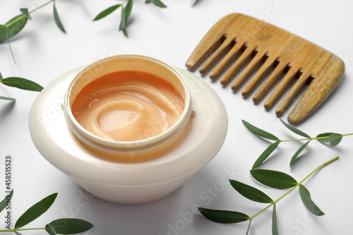 Jar of hair care cosmetic product, wooden comb and green leaves on white background, closeup