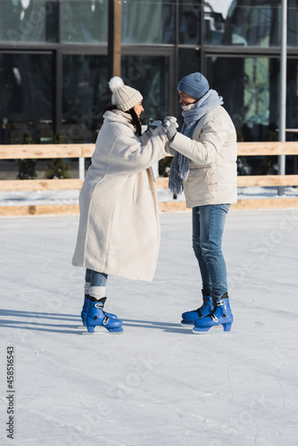 full length of happy couple skating on ice rink