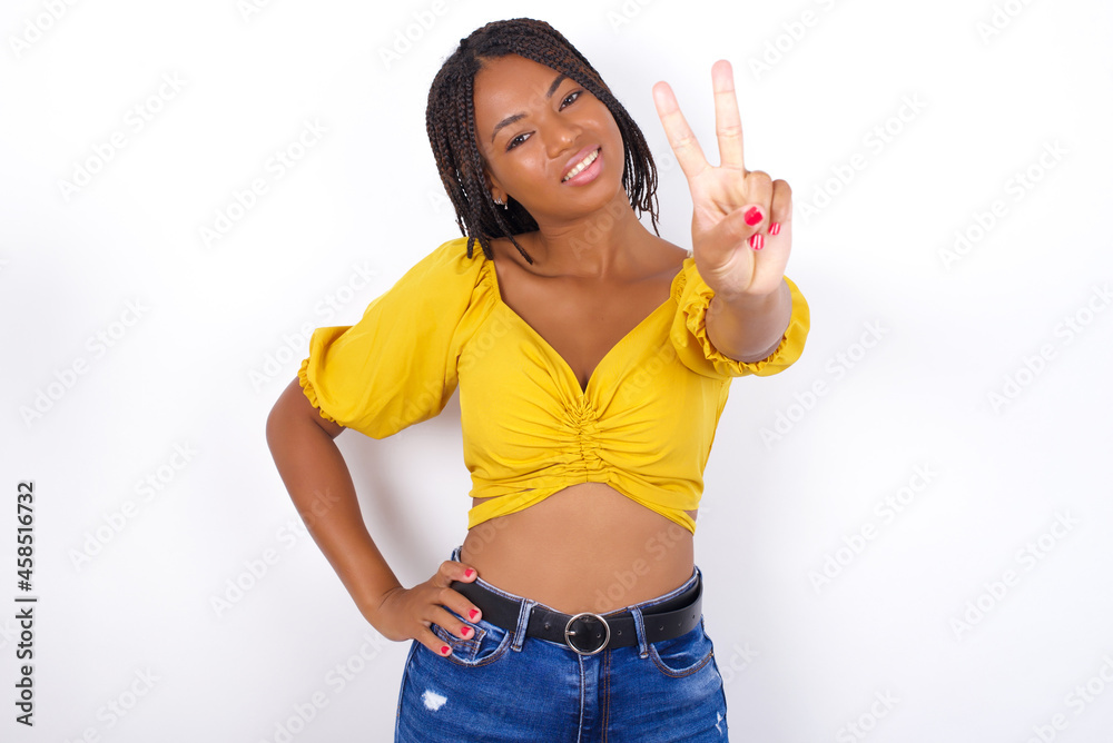 afro american woman with braids wearing sexy yellow t-shirt on white wall directs fingers at camera selects someone. I recommend you. Best choice afro american woman with braids wearing sexy yellow t-shirt on white wall directs fingers at camera selects someone. I recommend you. Best choice