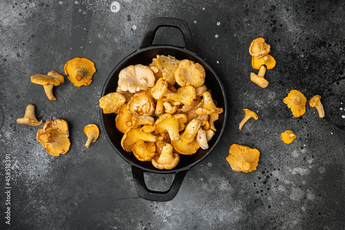 Chanterelle mushrooms, in cast iron frying pan, on black dark stone table background, top view flat lay