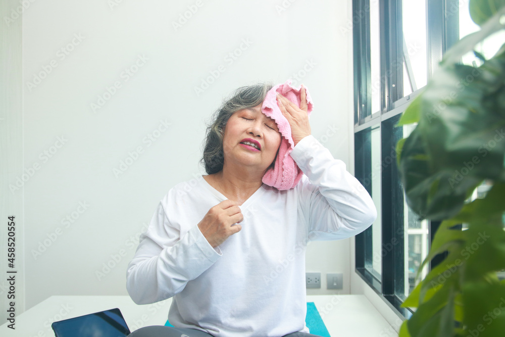Asian elderly woman exercising at home Take a pink cloth to wipe the sweat. Exercises to maintain health for the elderly. concept of social distancing